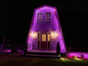 barn-style home with purple, blue and red permanent holiday lights