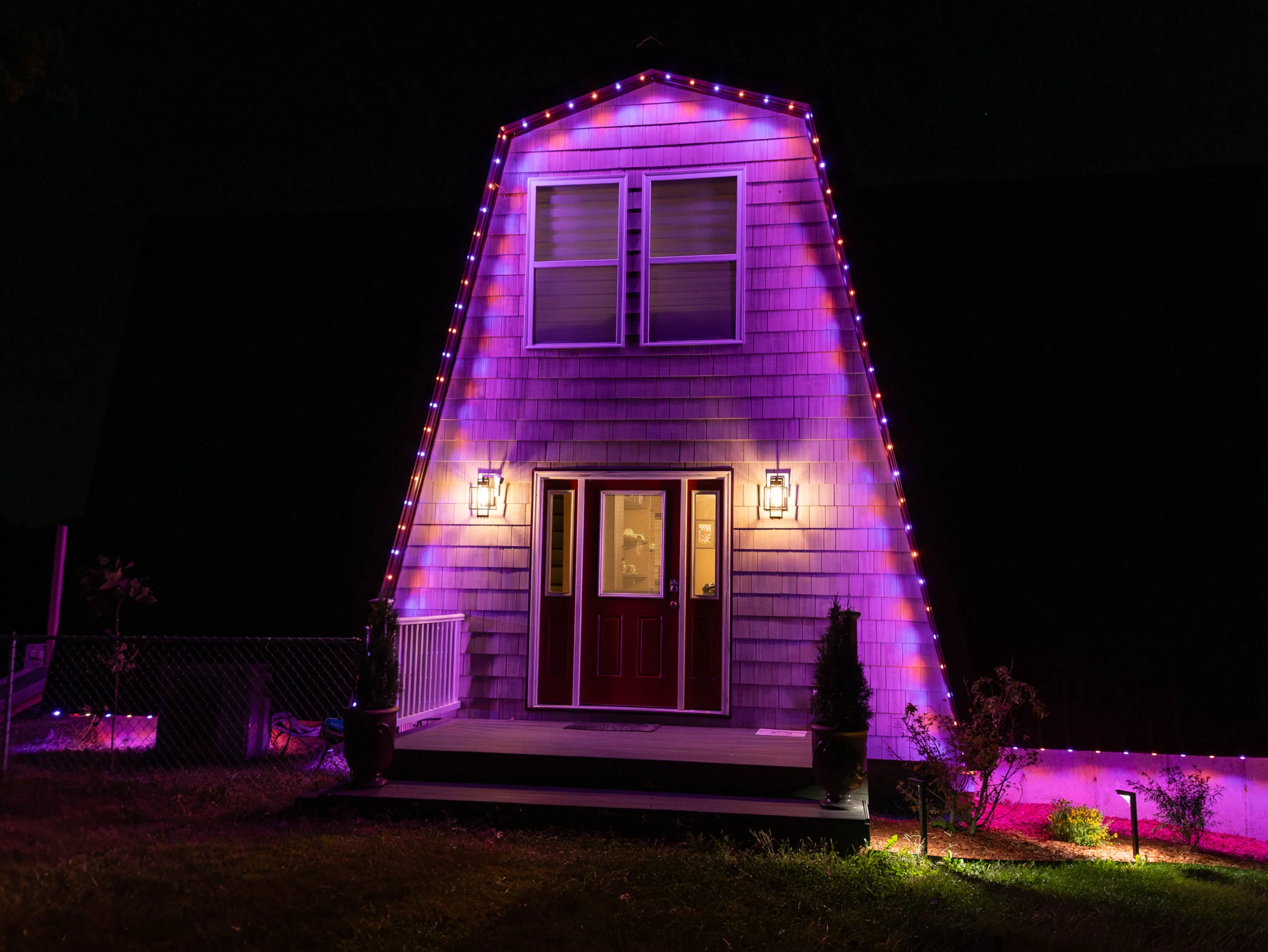 barn-style home with purple, blue and red permanent holiday lights